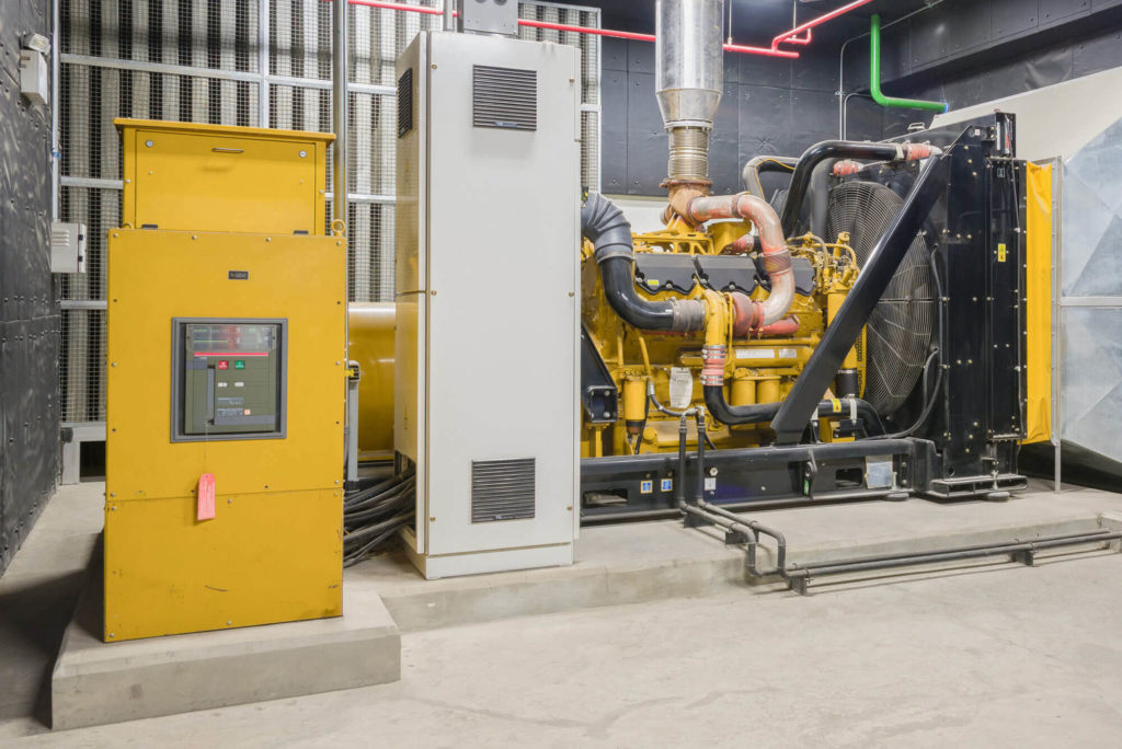 wideshot of yellow generator standing alone in a grey industrial room